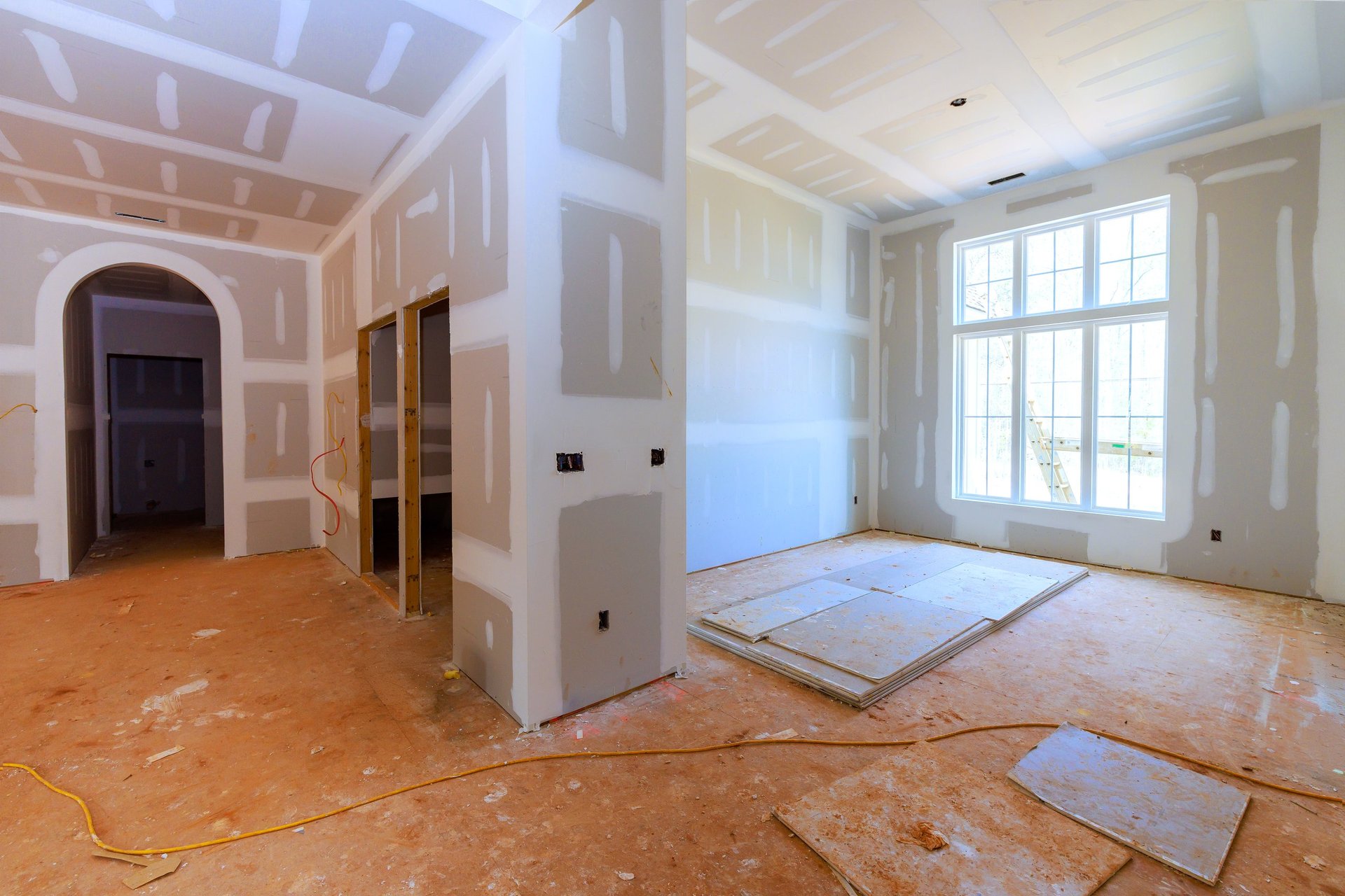 Workers are preparing new home interior with drywall, bare floors in room with large windows during construction